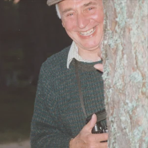 Derek Warren hiding behind a tree, laughing with his camera